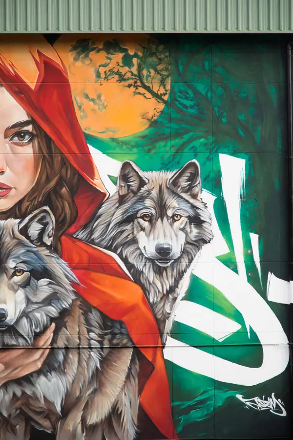 Detalle lateral del mural escolar con lobo y fondo verde durante el proceso de ejecución