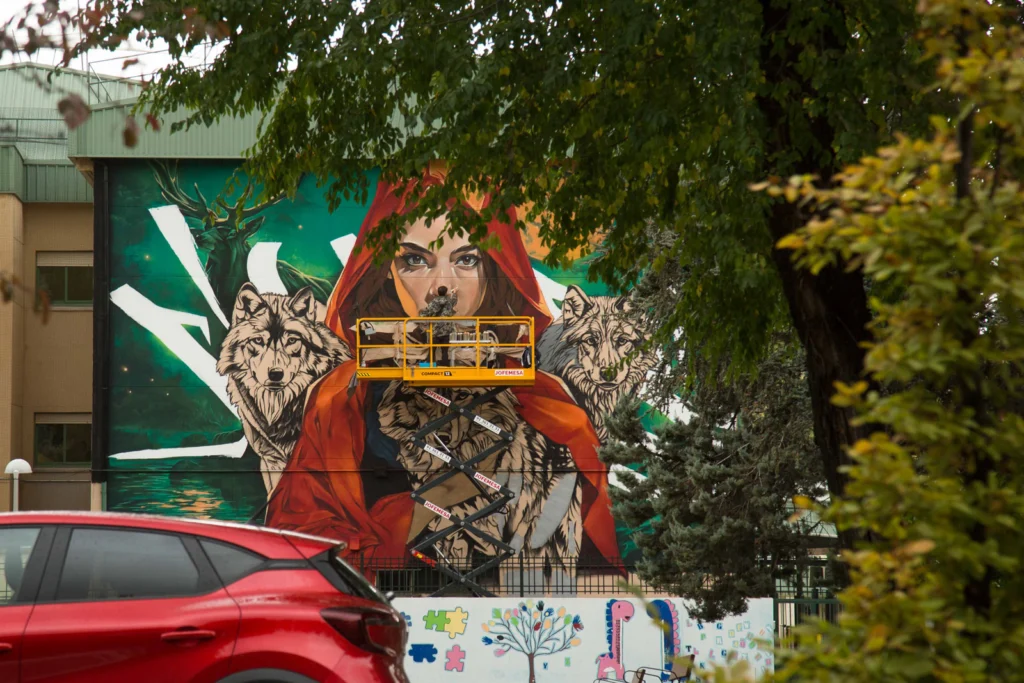 Proceso de pintura de mural escolar con elevadora en fachada de colegio en Madrid
