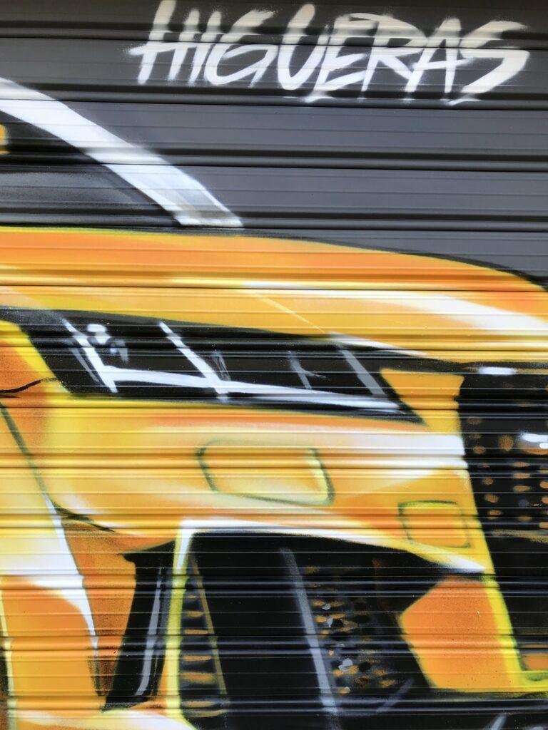 Detalle de coche deportivo amarillo pintado con graffiti en la persiana de GALA Autoescuela Higueras