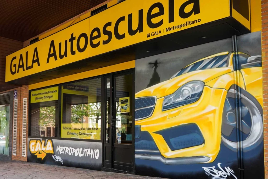 Mural con coche BMW amarillo en fachada de Autoescuela Gala Metropolitano