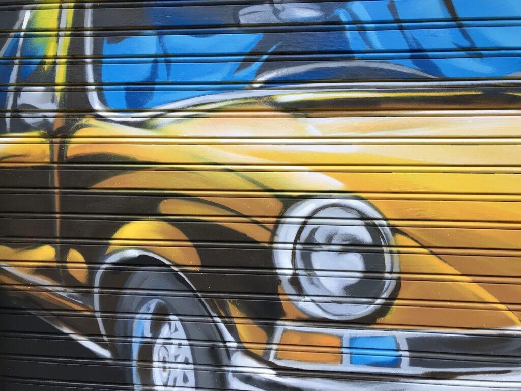 Detalle del coche clásico amarillo pintado en la persiana de GALA Autoescuela Mar de Cristal
