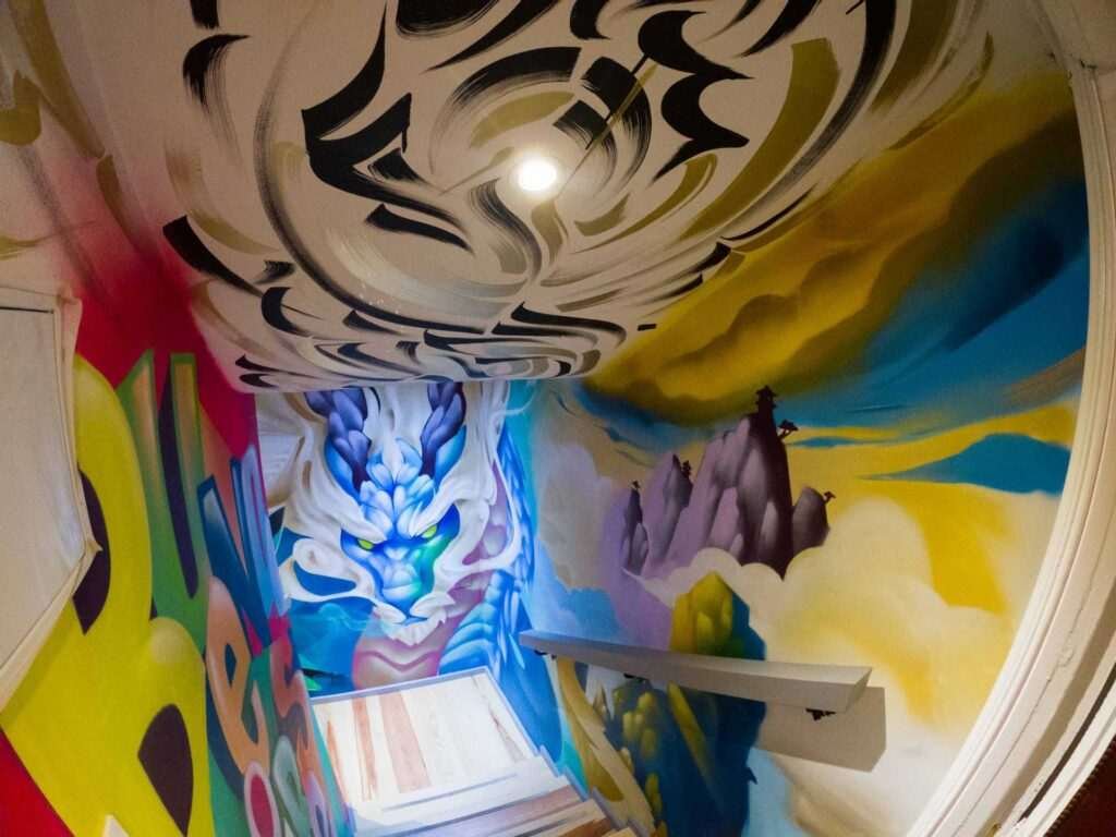 Graffiti interior con retratos y dragón en escalera de acceso a bodega