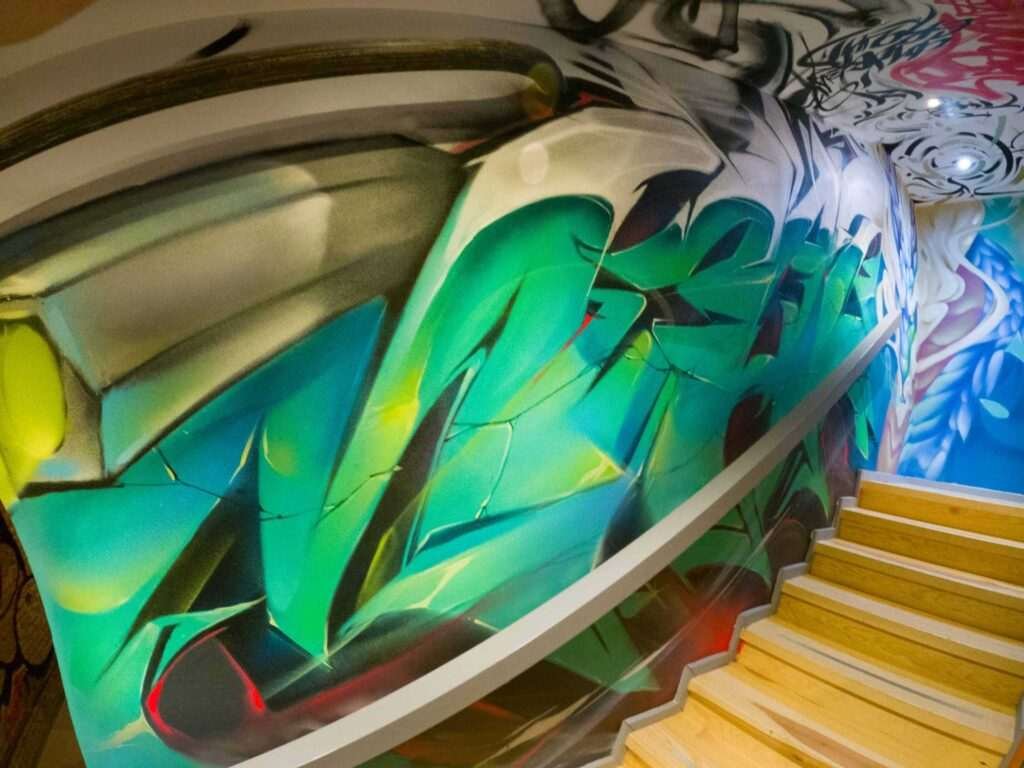 Graffiti interior con retratos y dragón en escalera de acceso a bodega