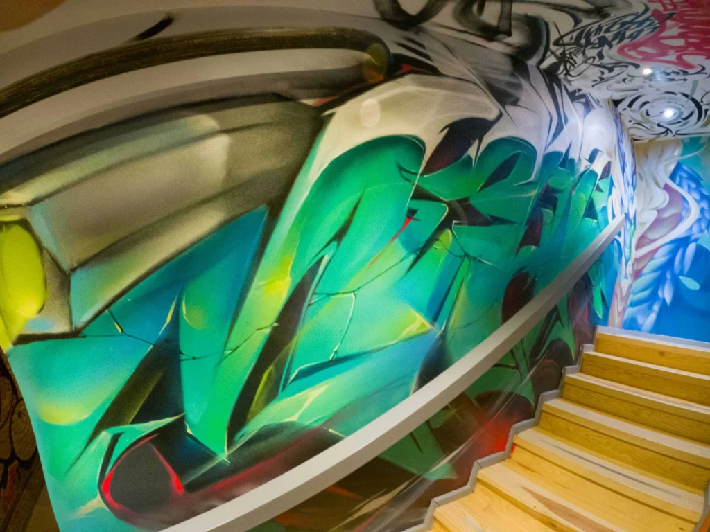 Graffiti interior con retratos y dragón en escalera de acceso a bodega