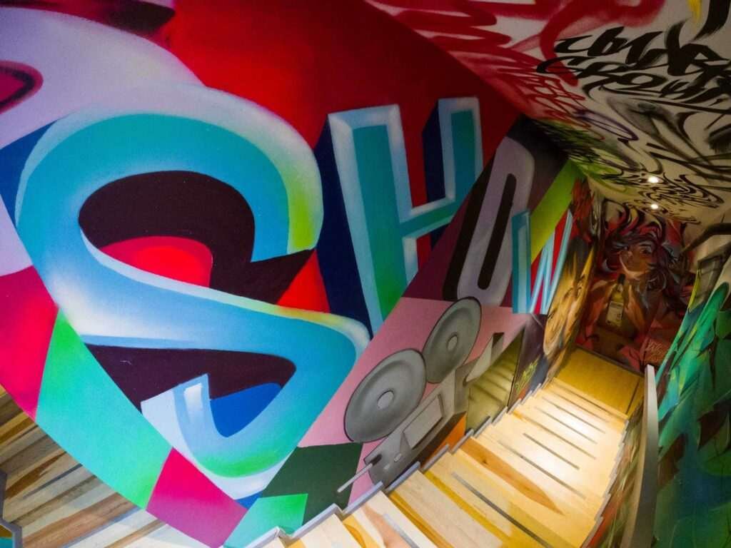 Graffiti interior con retratos y dragón en escalera de acceso a bodega