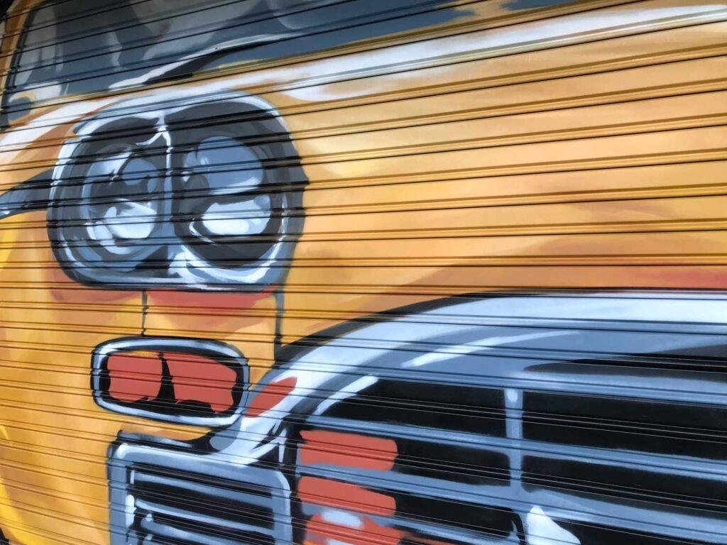 Coche clásico pintado en cierre de Autoescuela Gala Arturo Soria, graffiti realista