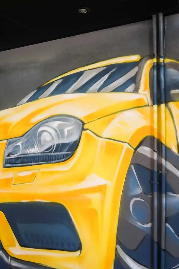 Mural con coche BMW amarillo en fachada de Autoescuela Gala Metropolitano