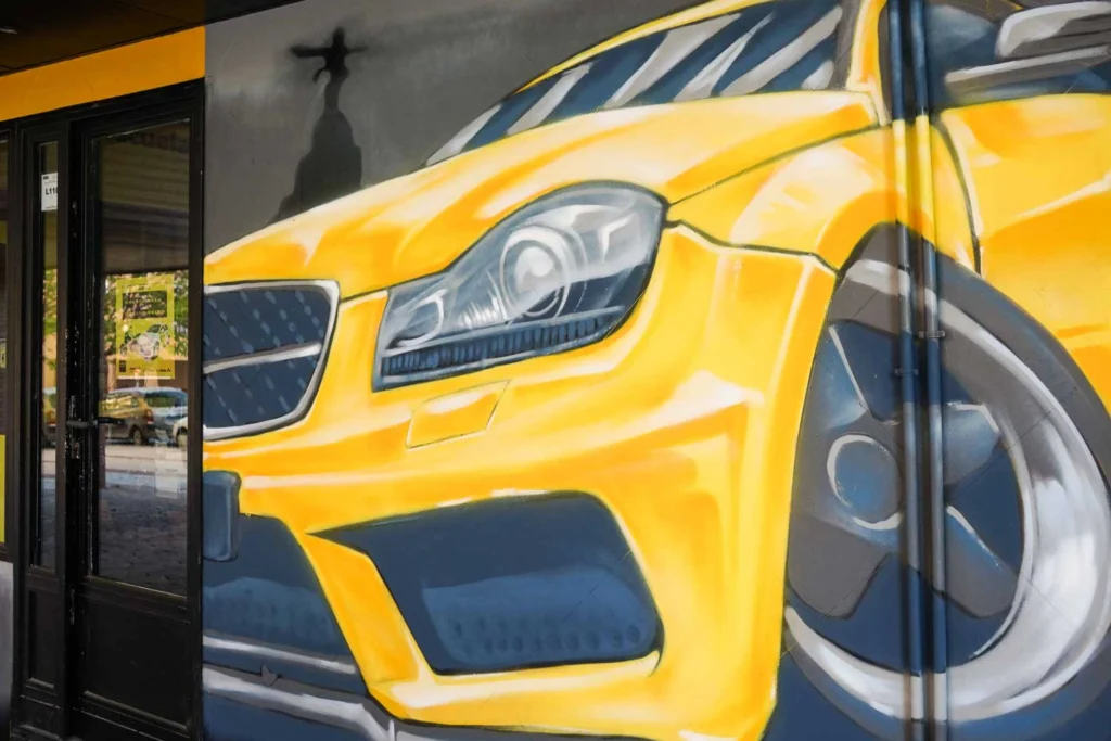 Mural con coche BMW amarillo en fachada de Autoescuela Gala Metropolitano