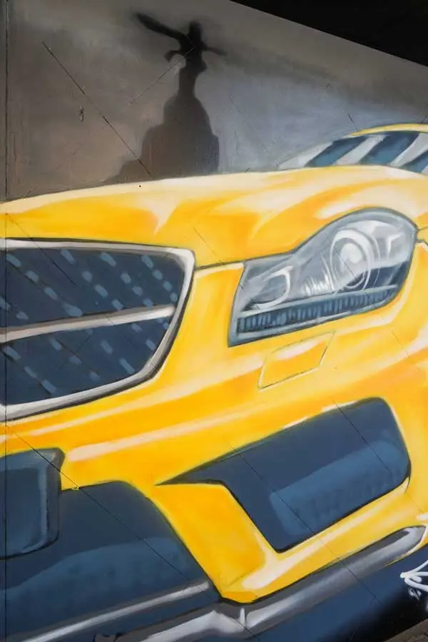 Mural con coche BMW amarillo en fachada de Autoescuela Gala Metropolitano