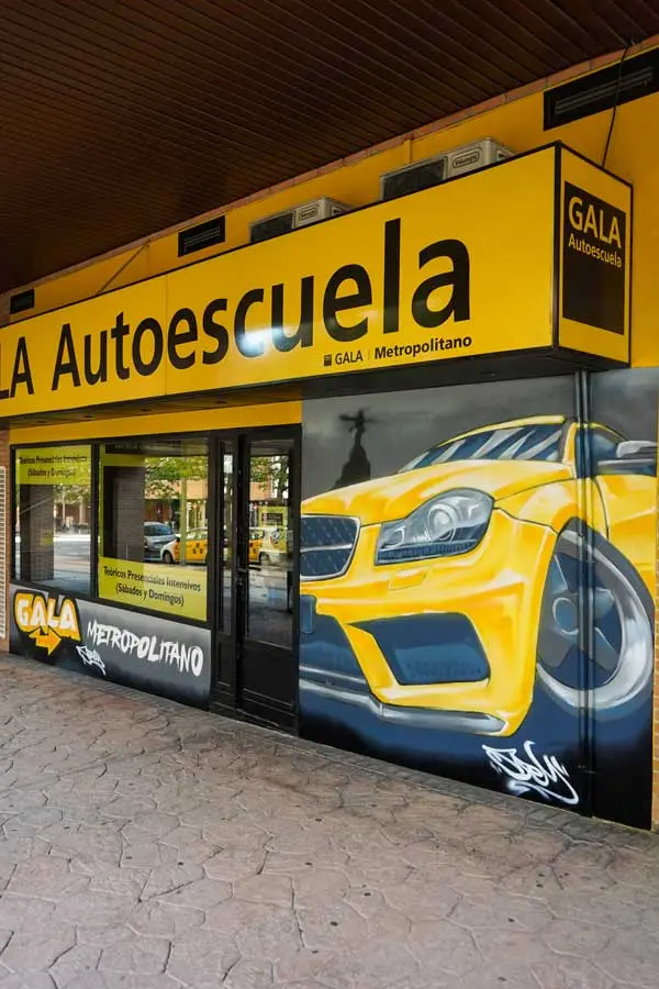Mural con coche BMW amarillo en fachada de Autoescuela Gala Metropolitano