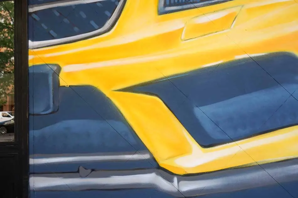 Mural con coche BMW amarillo en fachada de Autoescuela Gala Metropolitano