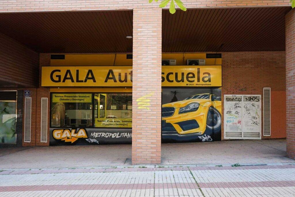 Mural con coche BMW amarillo en fachada de Autoescuela Gala Metropolitano