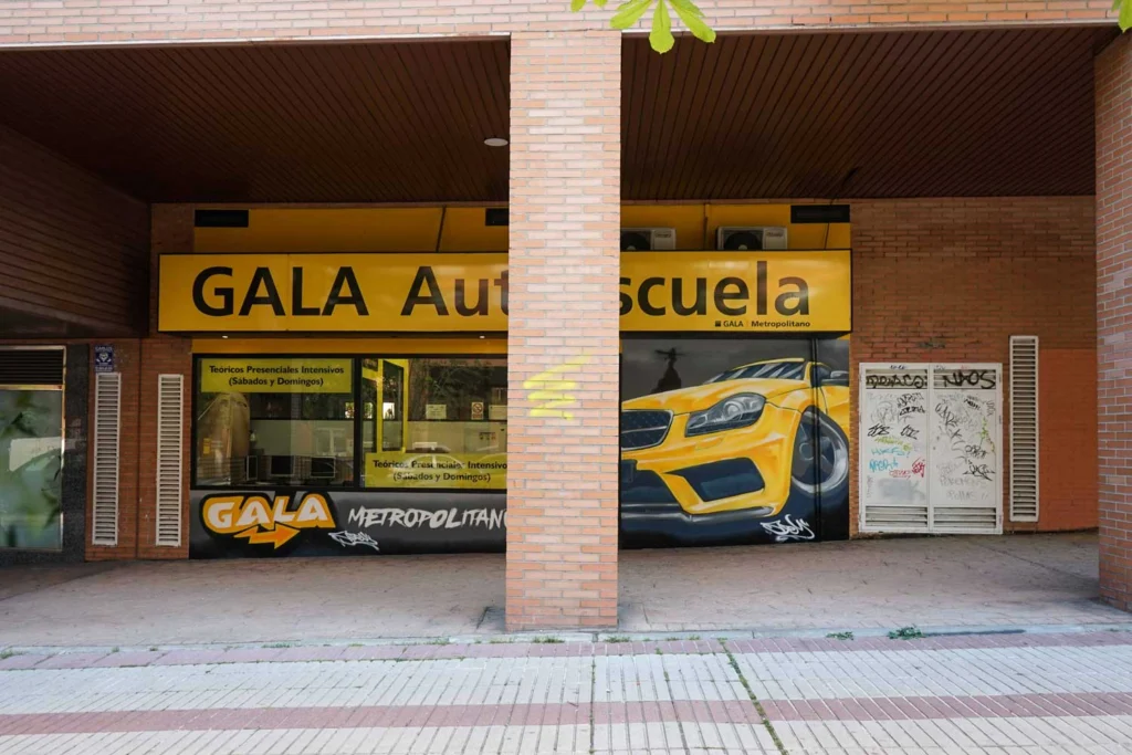 Mural con coche BMW amarillo en fachada de Autoescuela Gala Metropolitano