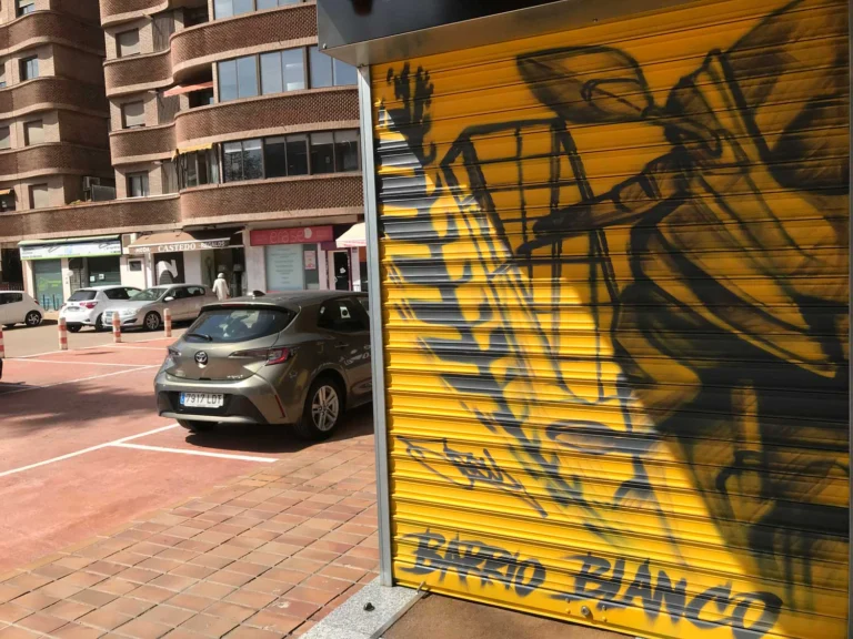 Mural con moto de carreras en cierre metálico del Barrio Blanco (Madrid), estilo urbano