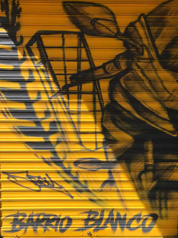 Mural con moto de carreras en cierre metálico del Barrio Blanco (Madrid), estilo urbano