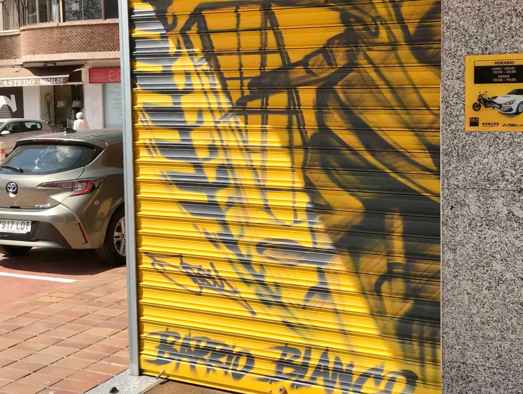 Mural con moto de carreras en cierre metálico del Barrio Blanco (Madrid), estilo urbano