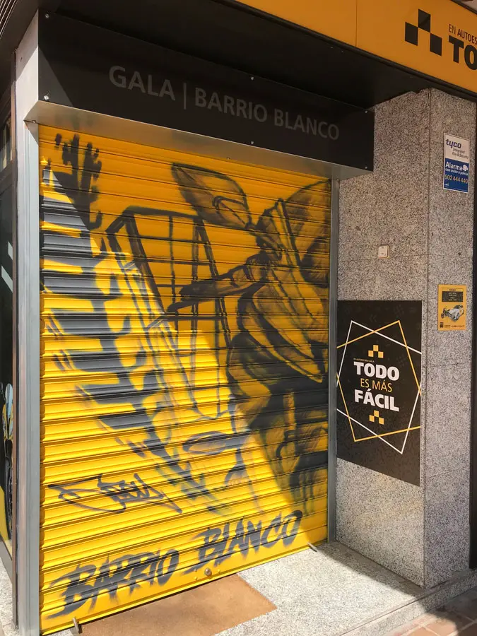 Mural con moto de carreras en cierre metálico del Barrio Blanco (Madrid), estilo urbano