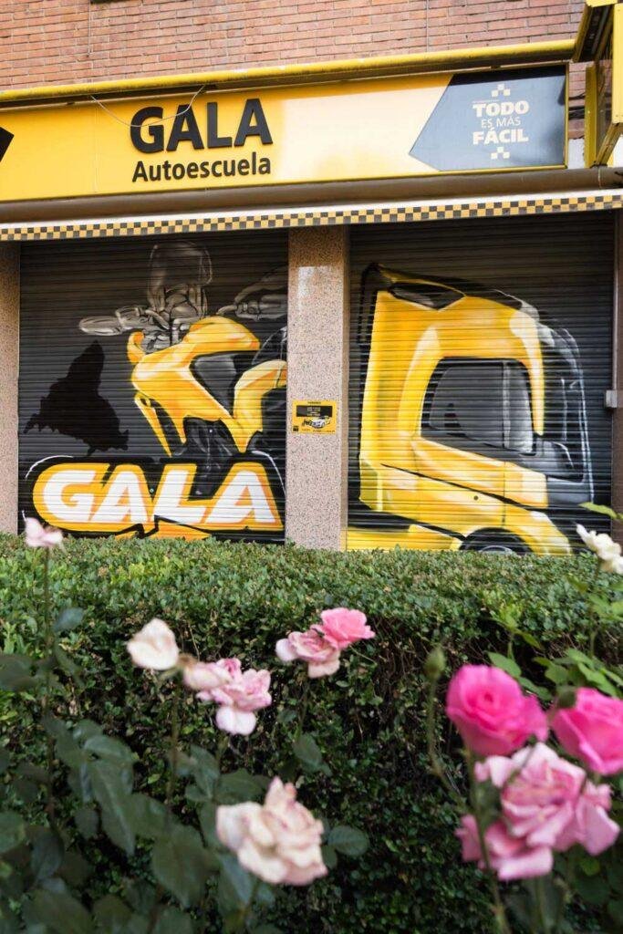 Cierre pintado de Autoescuela Gala con camión y moto en estilo urbano