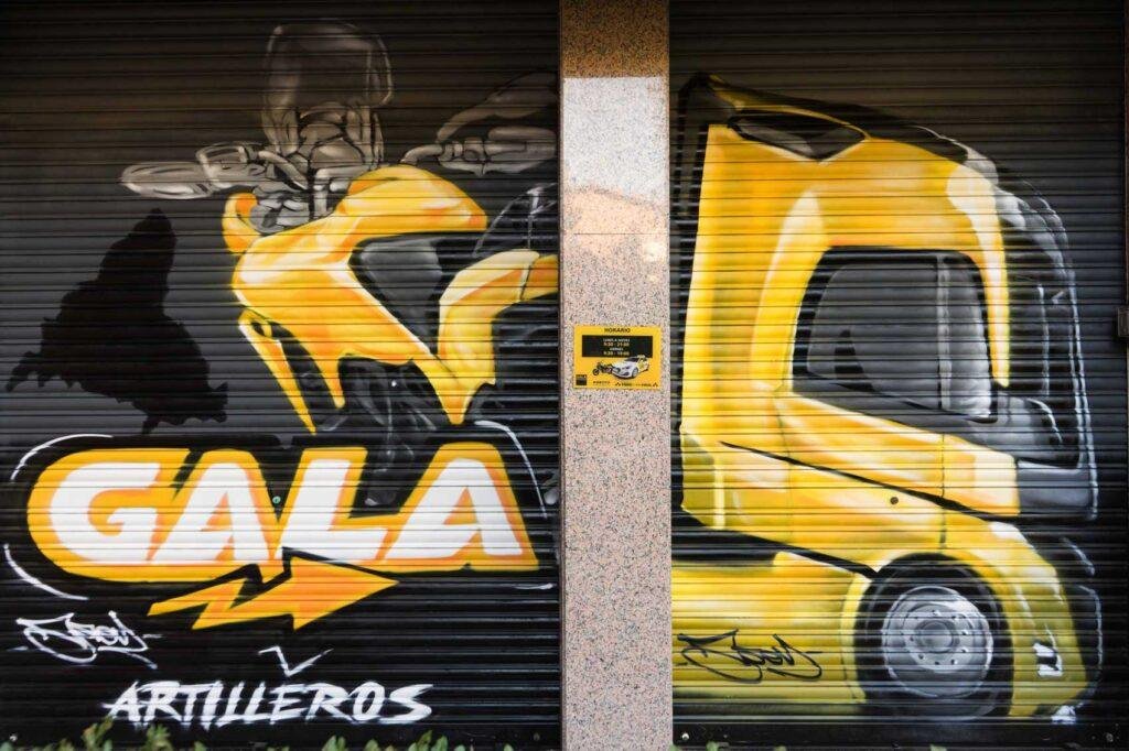 Cierre pintado de Autoescuela Gala con camión y moto en estilo urbano