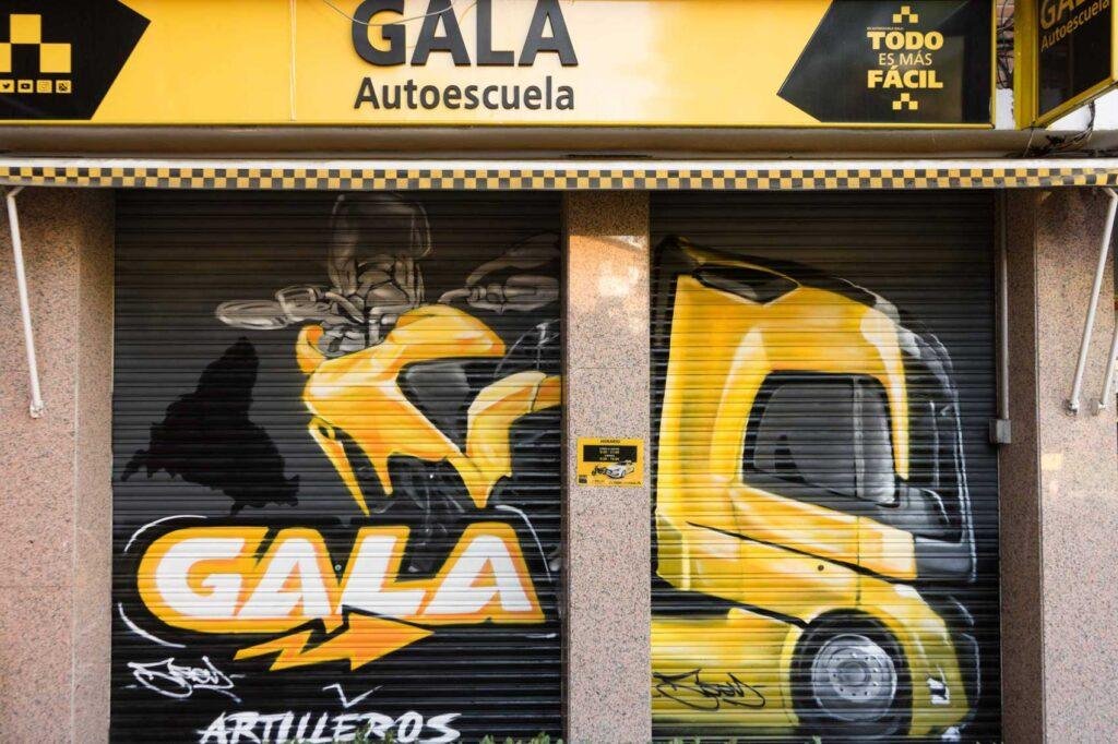 Cierre pintado de Autoescuela Gala con camión y moto en estilo urbano