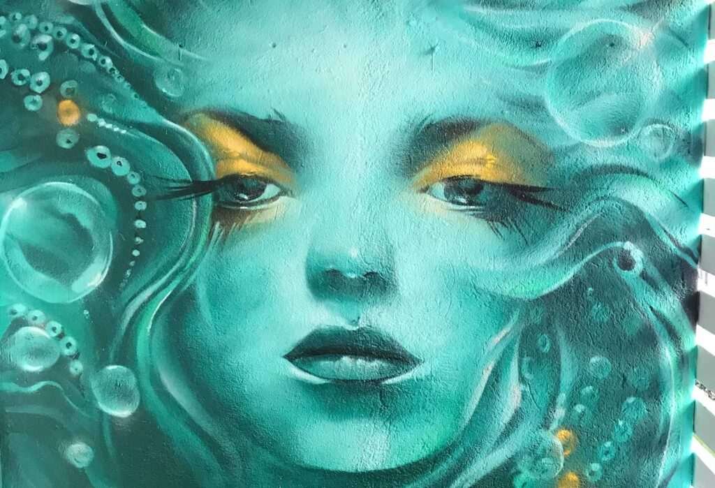 Mural urbano con rostro femenino turquesa en terraza interior