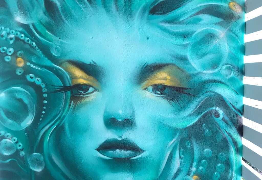 Mural urbano con rostro femenino turquesa en terraza interior