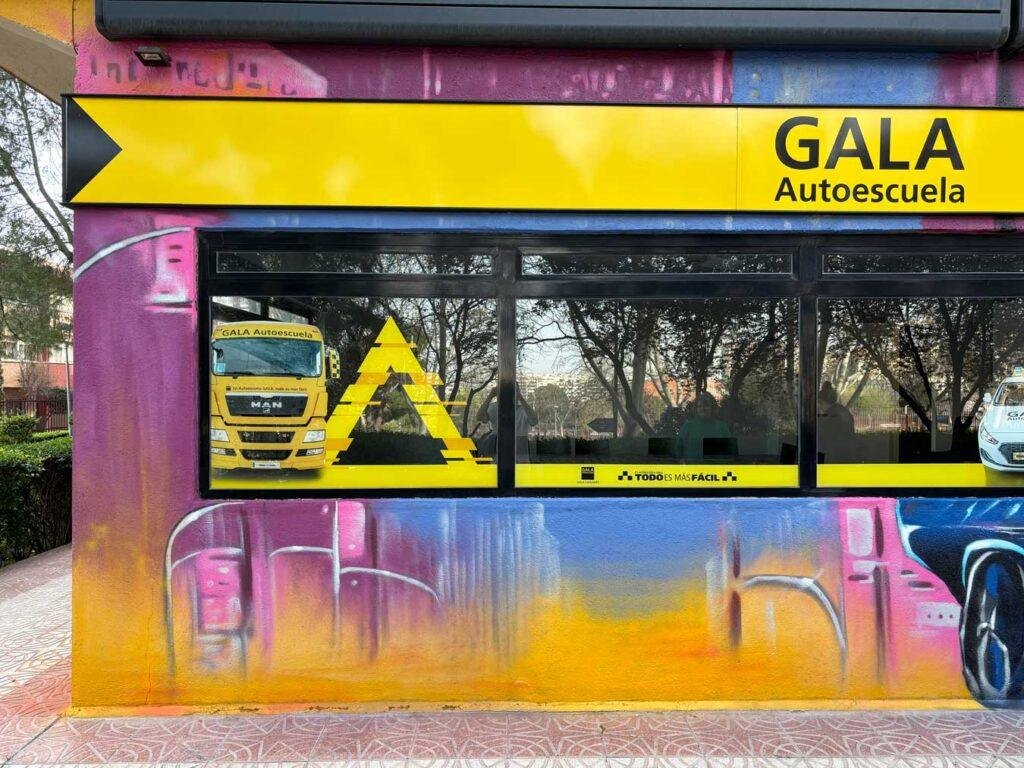 Fachada comercial de GALA Autoescuela en Móstoles decorada con mural de coches y motos