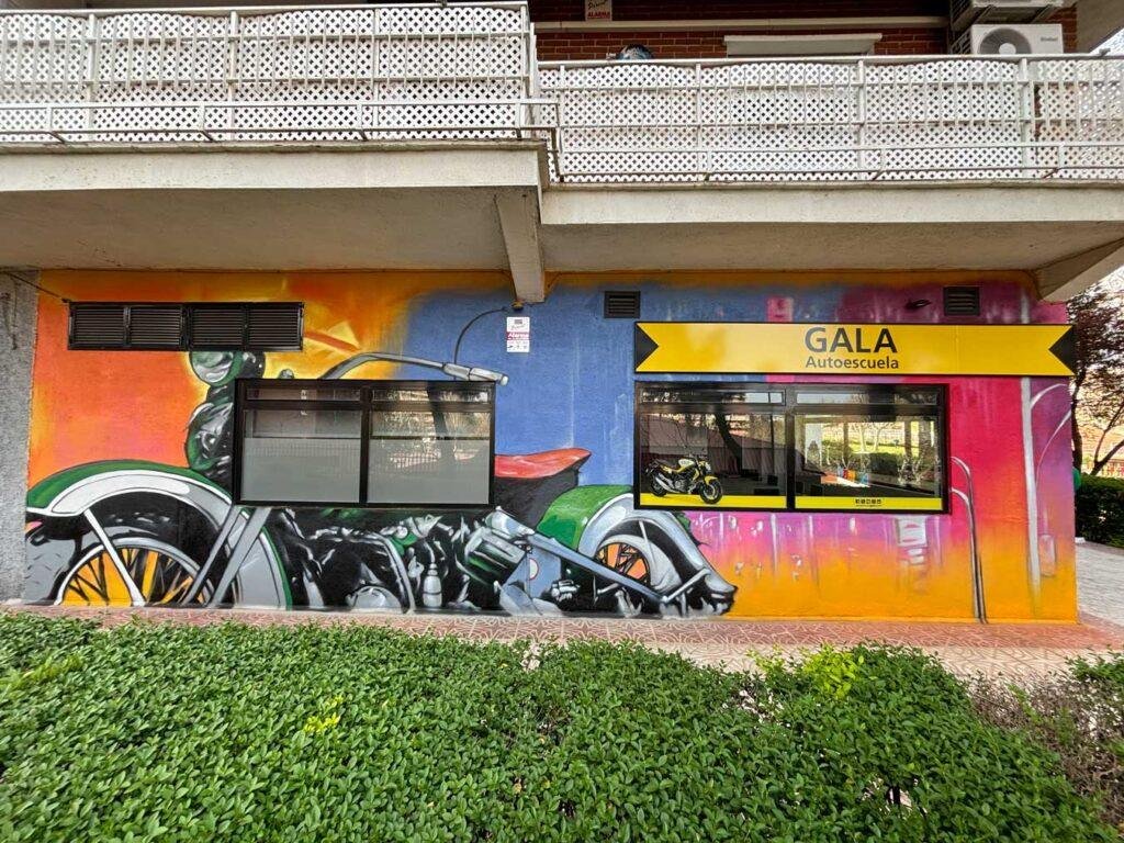 Panorámica del mural de fachada de GALA Autoescuela en Móstoles con coches, motos y rotulación