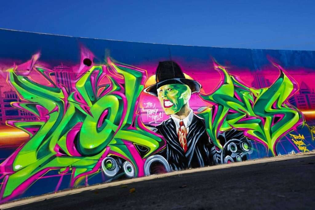 Mural de La Máscara estilo graffiti con fondo rosa y verde