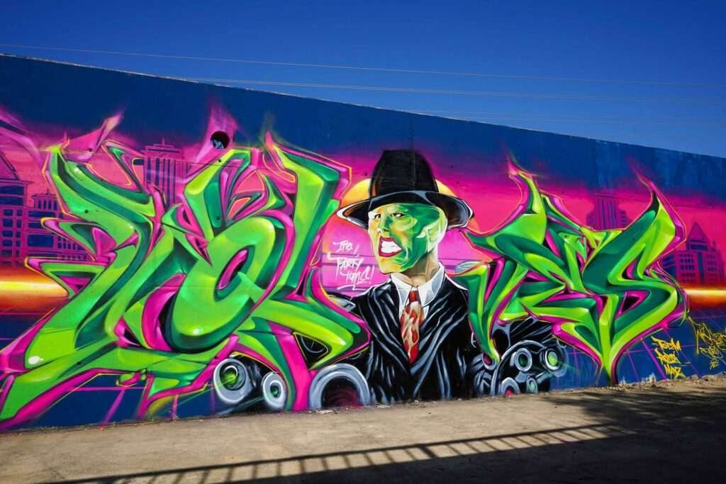 Mural de La Máscara estilo graffiti con fondo rosa y verde