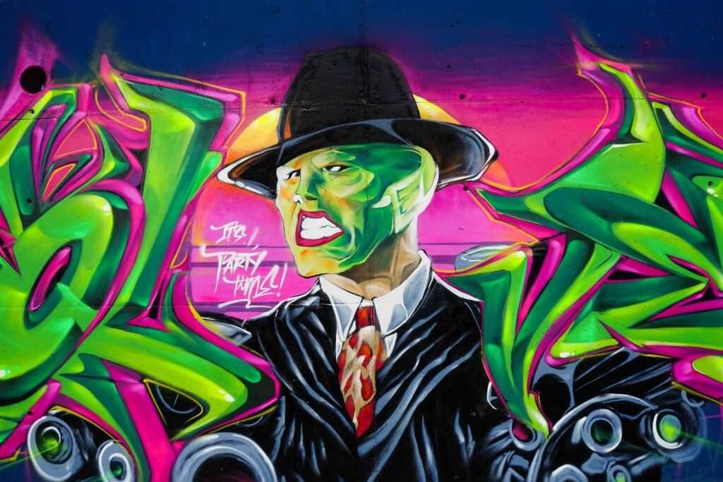 Mural de La Máscara estilo graffiti con fondo rosa y verde