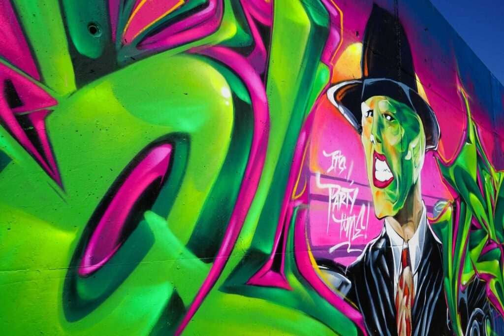 Mural de La Máscara estilo graffiti con fondo rosa y verde
