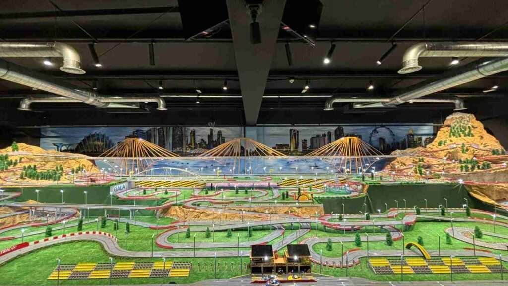 Vista completa de la maqueta Scalextric con mural de paisaje urbano en oficinas de GALA Autoescuela
