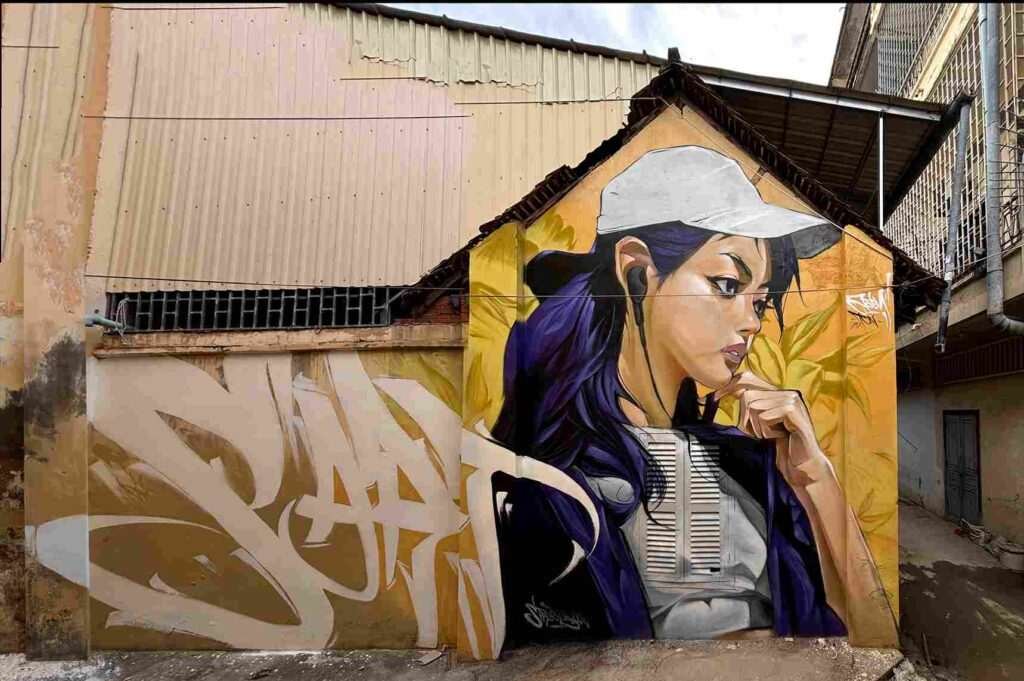 Mural graffiti en fachada de Camboya, retrato femenino con gorra para S’art Urban Art Festival.