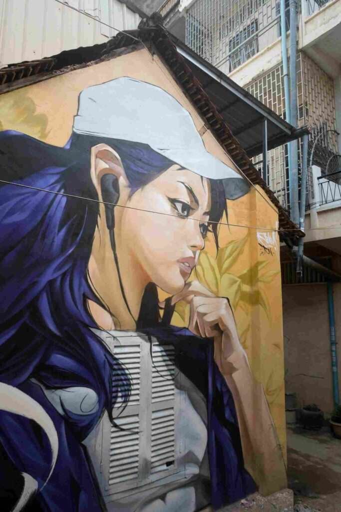 Mural graffiti en fachada de Camboya, retrato femenino con gorra para S’art Urban Art Festival.