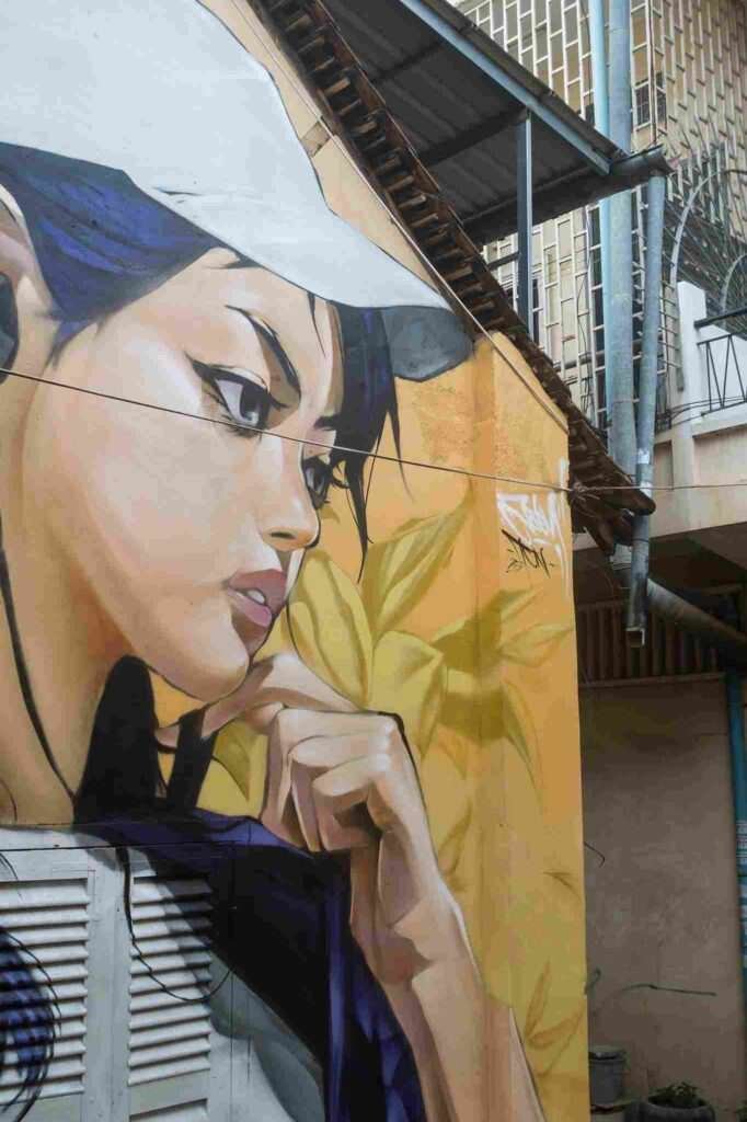 Mural graffiti en fachada de Camboya, retrato femenino con gorra para S’art Urban Art Festival.