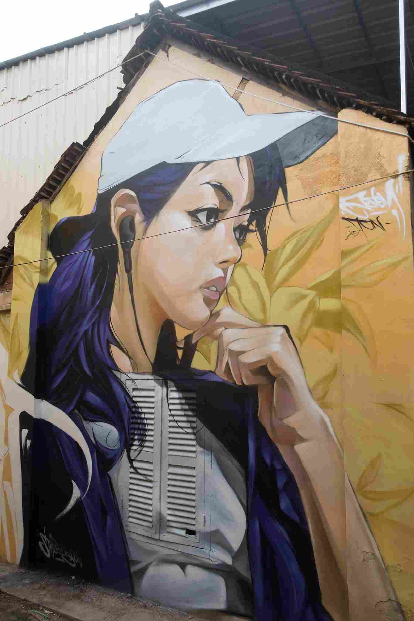 Mural graffiti en fachada de Camboya, retrato femenino con gorra para S’art Urban Art Festival.