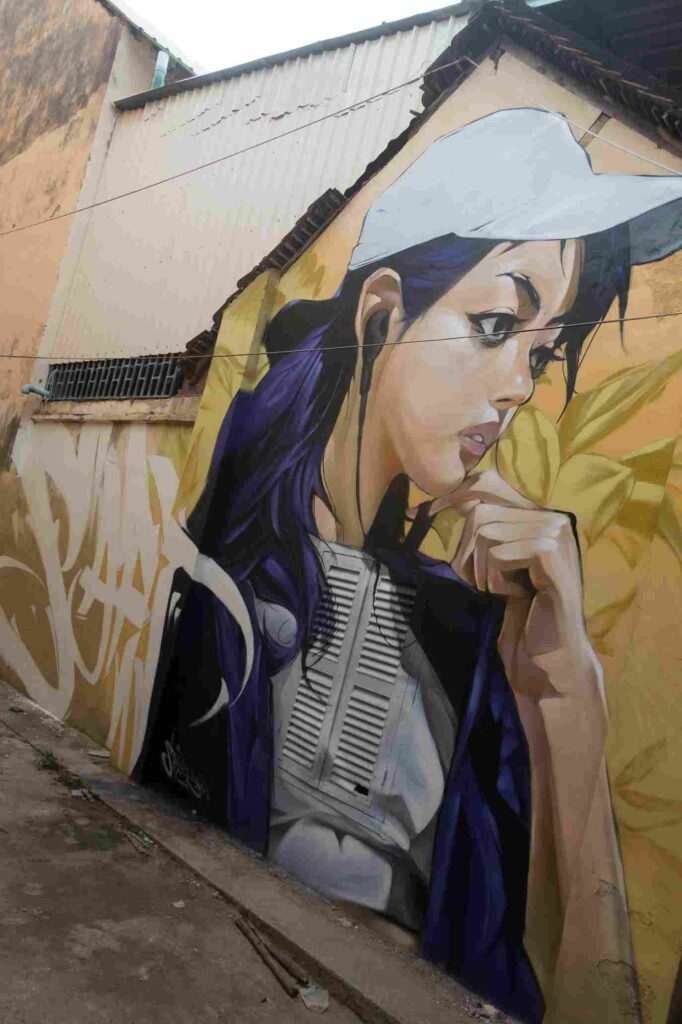 Mural graffiti en fachada de Camboya, retrato femenino con gorra para S’art Urban Art Festival.