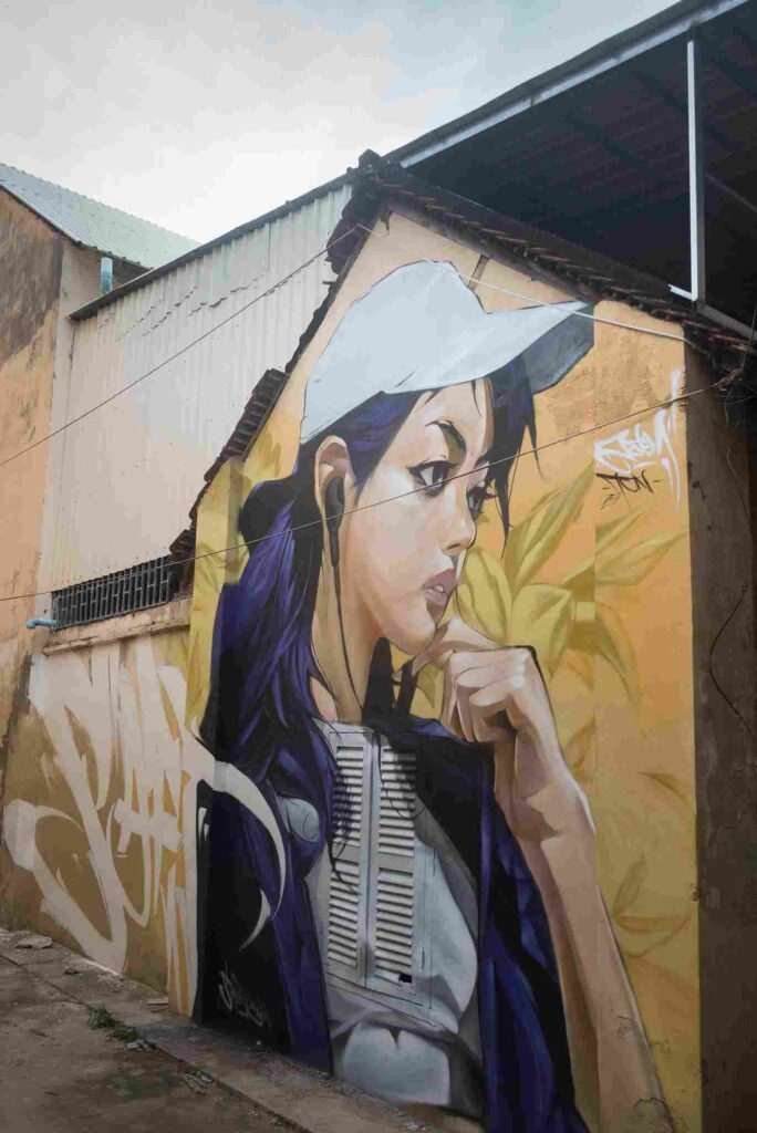 Mural graffiti en fachada de Camboya, retrato femenino con gorra para S’art Urban Art Festival.