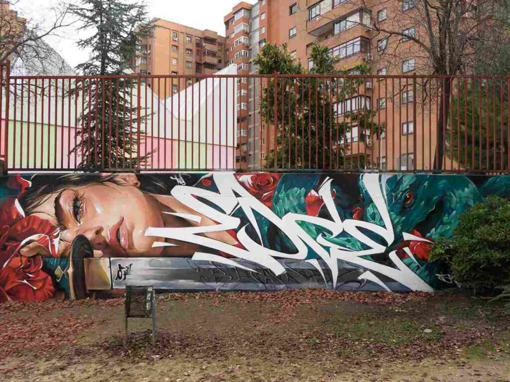 mural madrid the edge of the blade retrato femenino con rosas y serpiente tipografía graffiti blanca barrio del pilar