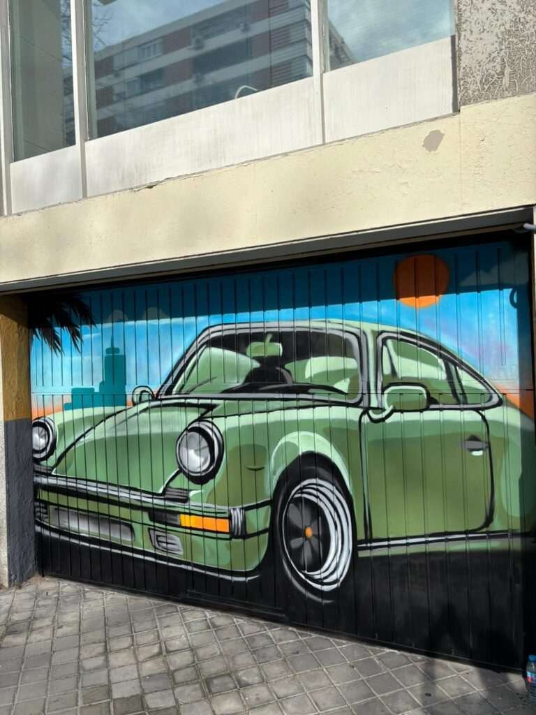 Detalle de mural graffiti en puerta de garaje con coche clásico verde y fondo azul