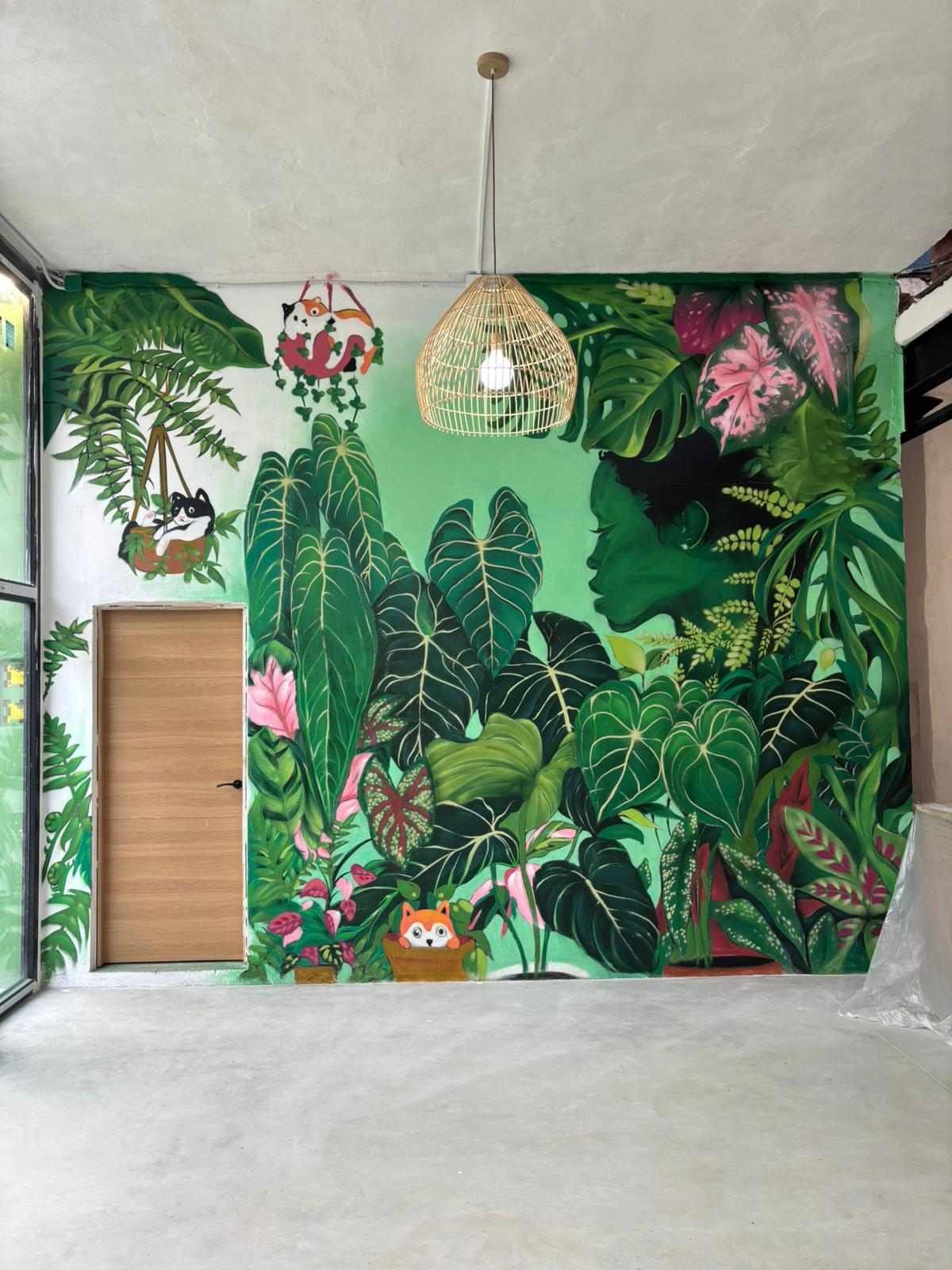 Mural de hojas tropicales en Torrelavega con composición vista a través de cerramiento negro interior