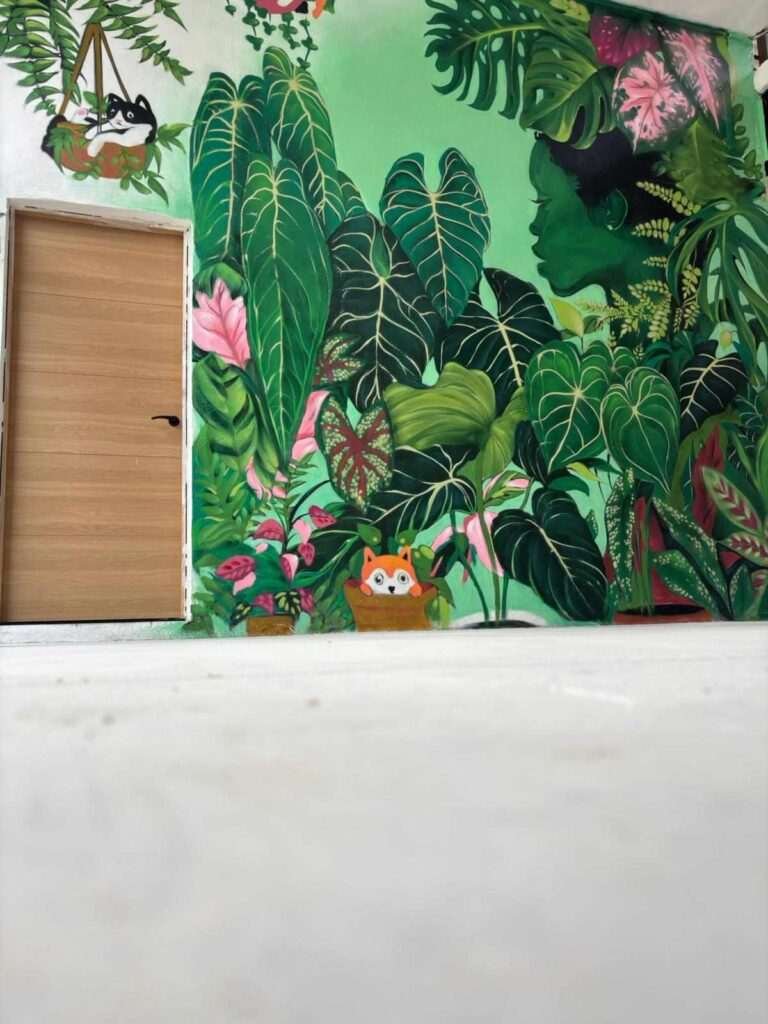 Detalle de mural botánico en Cantabria con grandes hojas verdes pintadas sobre pared interior