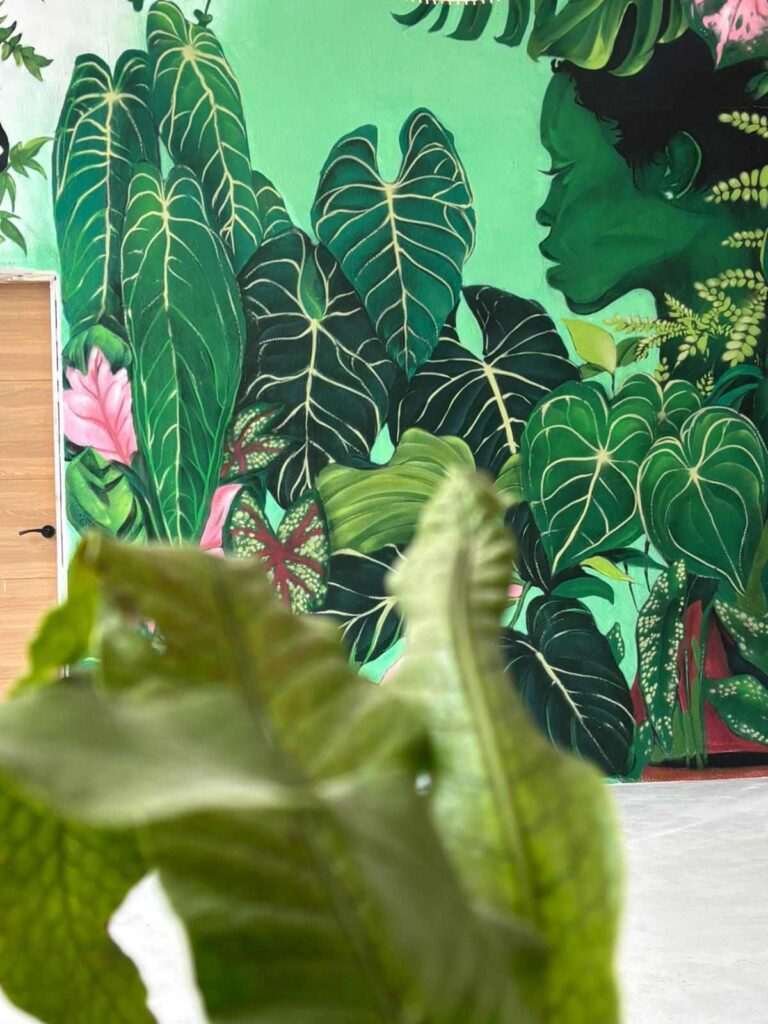 Mural vegetal en tienda Plantukas de Torrelavega con hojas tropicales y retrato femenino entre vegetación