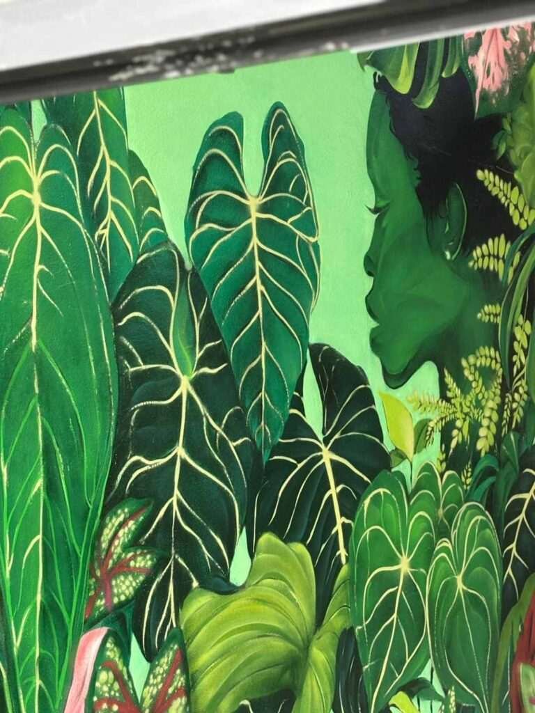 Detalle de mural vegetal en Torrelavega visto entre puertas negras con perfil femenino y hojas tropicales