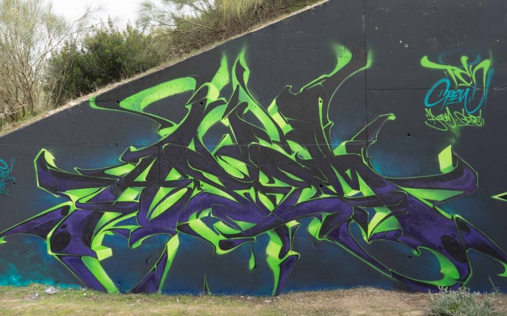Graffiti de letras en verde y morado sobre muro oscuro en Madrid Norte