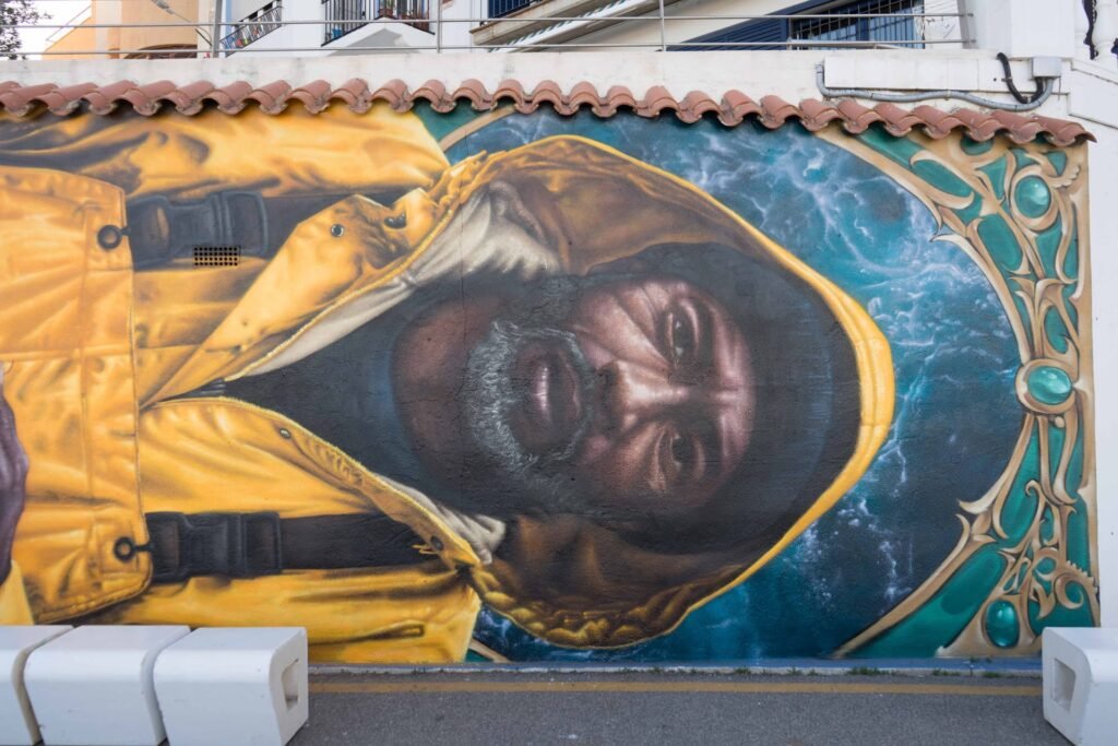 Retrato realista de un pescador con impermeable amarillo y sueste en el mural de l'Ametlla de Mar