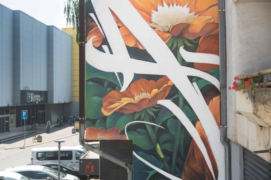 Detalle del mural Aroma en Bijeljina: flores naranjas, hojas oscuras y trazos caligráficos blancos