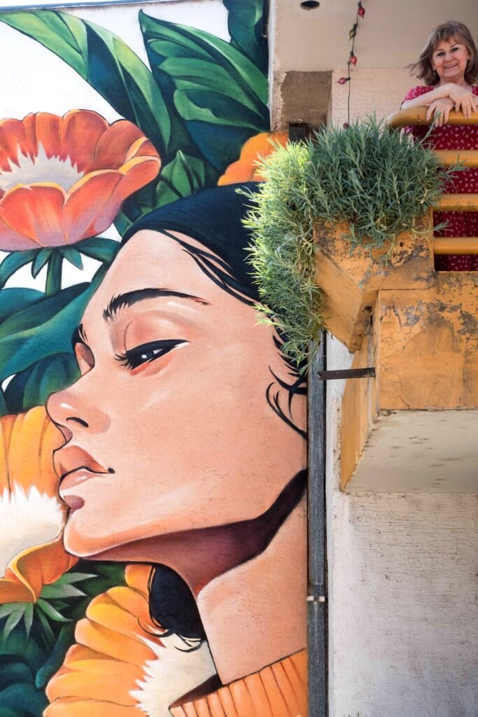 Detalle del rostro del mural Aroma: mujer de perfil acercando la cara a una flor naranja