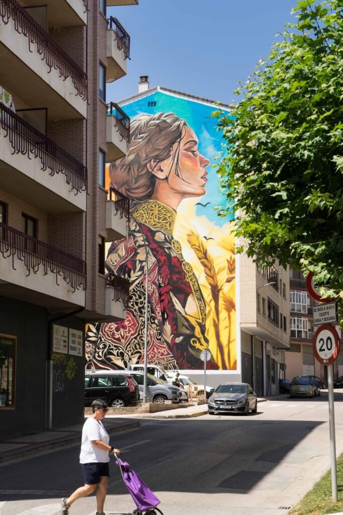 Perspectiva de calle del mural Casilda en Briviesca entre árboles y bloques de viviendas